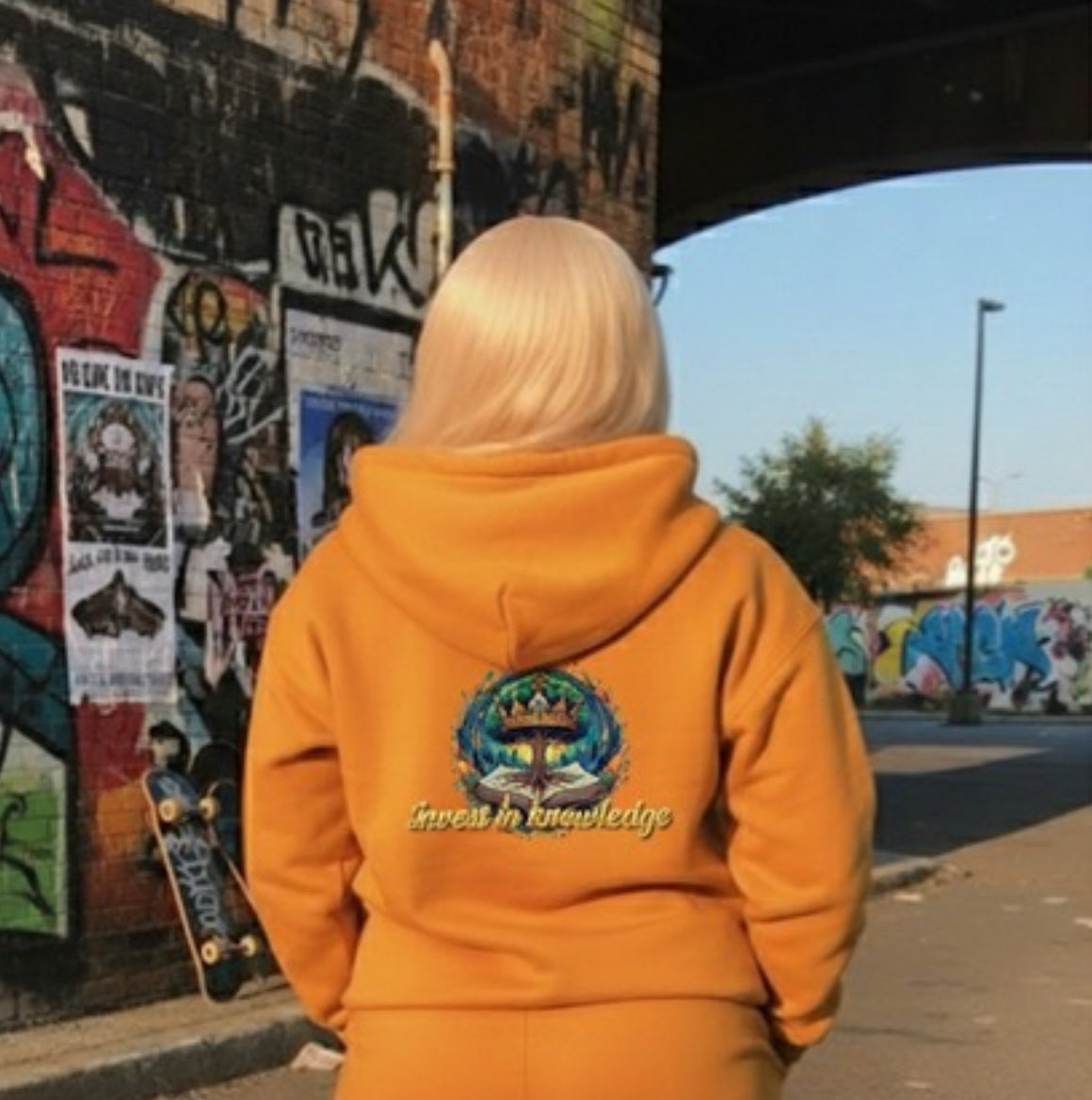 Invest In Knowledge- HOODIE worn by a model against a graffiti wall, showcasing streetwear style and vibrant color.
